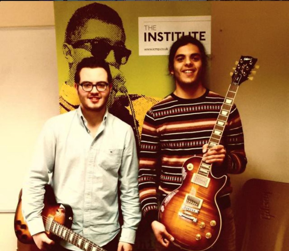 Théo Hénusse, on the left, and another scholarship winner receiving their Gibson guitars in front of the ICMP poster in London.